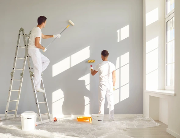 Two painters working on a wall, one standing on a steel staircase and the other on the floor